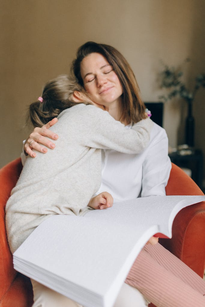 A mother and daughter share a loving embrace while reading a braille book.